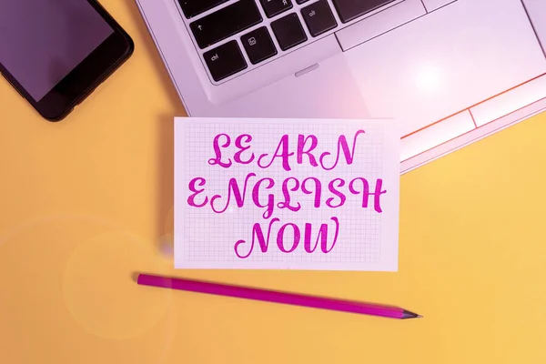 Text sign showing Learn English Now. Conceptual photo gain or acquire knowledge and skill of english language Metallic laptop pencil squared paper sheet smartphone colored background.