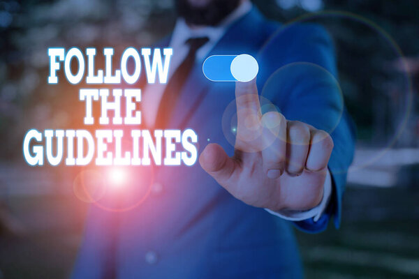 Text sign showing Follow The Guidelines. Conceptual photo Manual of Style Follow a Specified Rule Accordingly Male human wear formal work suit presenting presentation using smart device.