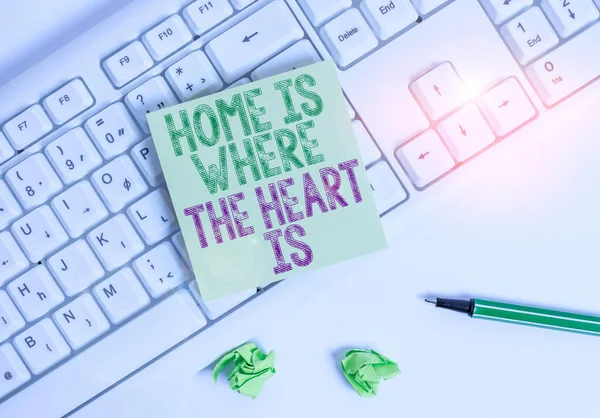 Note d'écriture montrant Home Is Where The Heart Is. Photo d'affaires montrant votre maison est où vous vous sentez à l'aise et heureux Papier de note vert avec crayon sur fond blanc et clavier PC . — Photo