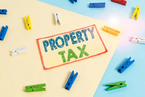 Writing note showing Property Tax. Business photo showcasing an ad valorem tax on the value of a property Millage rate Colored clothespin paper reminder with yellow blue background.