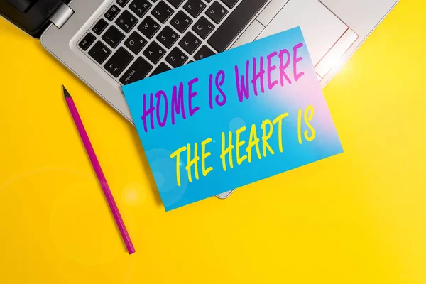 Ecriture conceptuelle montrant Home Is Where The Heart Is. Photo d'affaires mettant en valeur votre maison est où vous vous sentez à l'aise et heureux ordinateur portable métallique petit papier feuille crayon fond coloré . — Photo