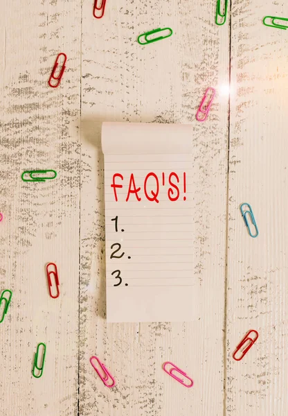 Text sign showing Faq. Conceptual photo a list of questions and answers relating to a particular subject Stripped ruled notepad clips lying wooden old retro vintage background.