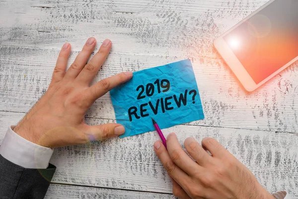 Text sign showing 2019 Review Question. Conceptual photo remembering past year events main actions or good shows Hand hold note paper near writing equipment and modern smartphone device. — Stok fotoğraf
