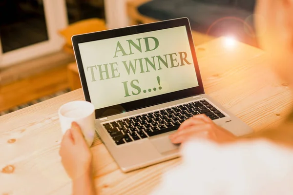 Handwriting text writing And The Winner Is. Concept meaning announcing who got first place at competition or exam woman laptop computer smartphone mug office supplies technological devices. — Stock Photo, Image
