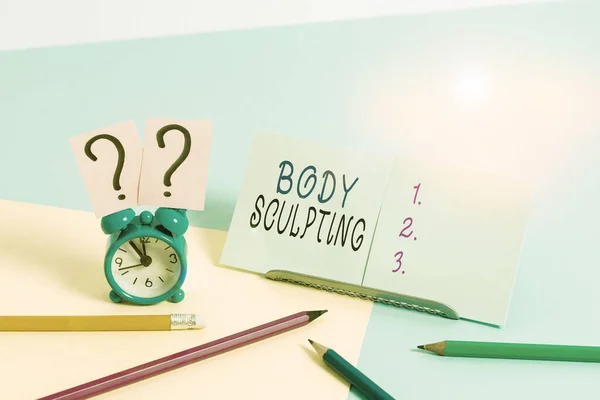 Writing note showing Body Sculpting. Business photo showcasing activity of increasing the body s is visible muscle tone Mini size alarm clock beside stationary on pastel backdrop.