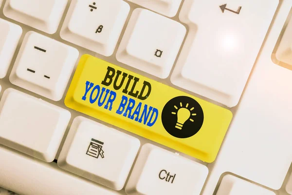 Text sign showing Build Your Brand. Conceptual photo enhancing brand equity using advertising campaigns White pc keyboard with empty note paper above white background key copy space.