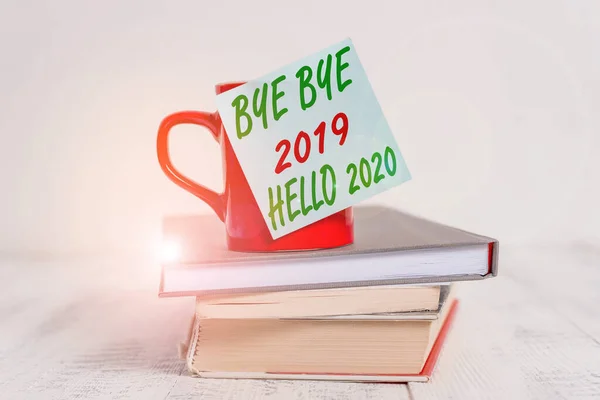 Scrivere a mano concettuale mostrando Ciao ciao 2019 Ciao 2020. Business photo text dicendo addio all'anno scorso e dando il benvenuto a un altro buon caffè appiccicoso tazza nota accatastati libri retrò vecchio tabl in legno retrò — Foto Stock