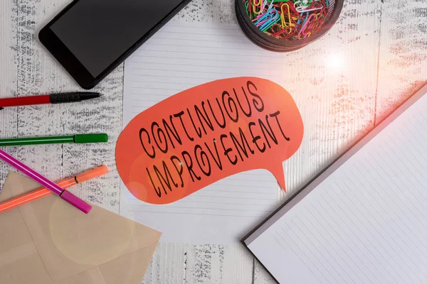 Tekst schrijven Continuous Improvement. Zakelijk concept voor voortdurende inspanning om producten of processen te verbeteren Smartphone pennen envelop clips spraakbellenvel notebook houten rug. — Stockfoto