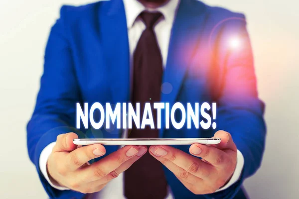 Scrivere testi a mano Nominations. Concetto che significa azione di nomina o stato di essere nominato per il premio Uomo d'affari in suite blu con una cravatta tiene lap top in mano . — Foto Stock