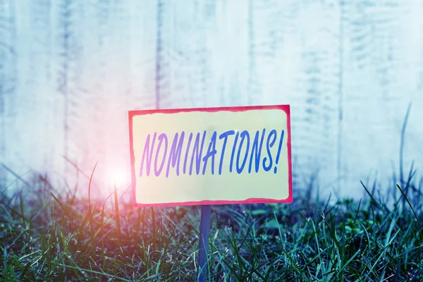 Writing note showing Nominations. Business photo showcasing action of nominating or state being nominated for prize Plain paper attached to stick and placed in the grassy land. — Stock Photo, Image