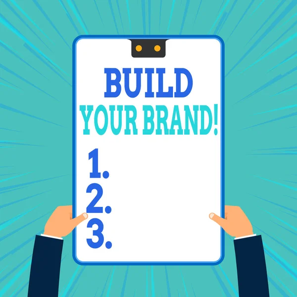 Εννοιολογική γραφή χέρι δείχνει Build Your Brand. Business photo text δημιουργεί ή βελτιώνει τη γνώση των πελατών και τις απόψεις του προϊόντος Δύο αρσενικά χέρια που κατέχουν ηλεκτρονική συσκευή γεωμετρικό υπόβαθρο. — Φωτογραφία Αρχείου