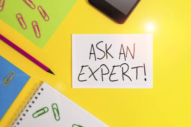 Ask An Expert 'ı gösteren bir not yazıyorum. İş fotoğrafı gösterme doğrulaması okudu ve kılavuz ilkelerini anladı ve kabul etti Kağıt kağıtlar kare defter kalem raptiyeleri akıllı telefon renkli arkaplan.
