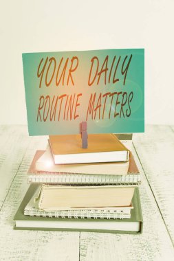 Günlük rutininizi yazan el yazısı metinleri. Kavram demek, düzenli olarak düzenli olarak bir şeyler yapmak demek yığınla kitap yığını, toka, toka, hatırlatıcı renkli beyaz ahşap..