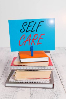 Kişisel Bakım 'ın el yazısı. Kavram demek, kişinin kendi sağlığını iyileştirmek için harekete geçmesi demektir. Yığınla kitap yığını, çamaşır mandalı, hatırlatıcı renkli beyaz ahşap..