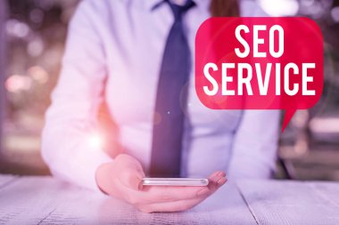 Seo Servisini gösteren bir not yazıyorum. İnternet sitesinin görünürlüğünü arttırmak için iş fotoğrafı gösterme teknikleri ve prosedürleri masaya oturan ve cep telefonu tutan kadın işadamı.