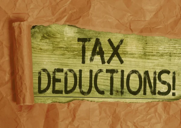 Conceptual hand writing showing Tax Deductions. Business photo showcasing reduction income that is able to be taxed of expenses Cardboard which is torn placed above a wooden classic table.