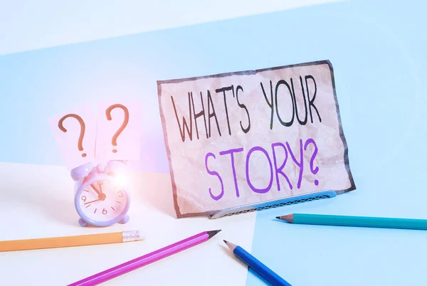 Writing note showing What S Your Story Question. Business photo showcasing asking demonstrating about his past life actions career or events Mini size alarm clock beside stationary on pastel backdrop. — 图库照片