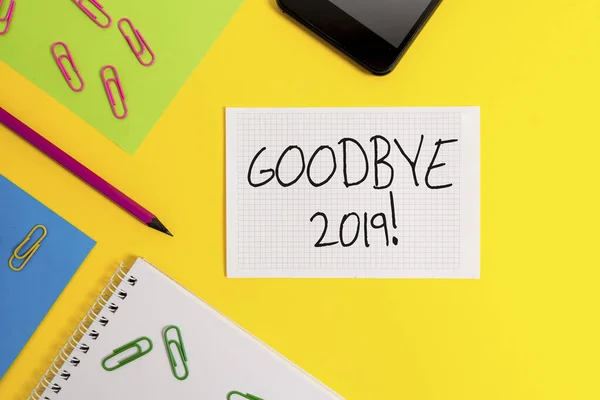 Writing note showing Good Bye 2019. Business photo showcasing express good wishes when parting or at the end of last year Paper sheets square notebook pencil clips smartphone colored background.