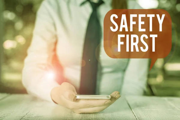 Writing note showing Safety First. Business photo showcasing used to say that the most important thing is to be safe Female business person sitting by table and holding mobile phone.