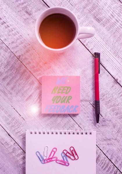 Conceptual hand writing showing We Need Your Feedback. Business photo showcasing criticism given to say can be done improvement Stationary placed next to a coffee cup above wooden table.