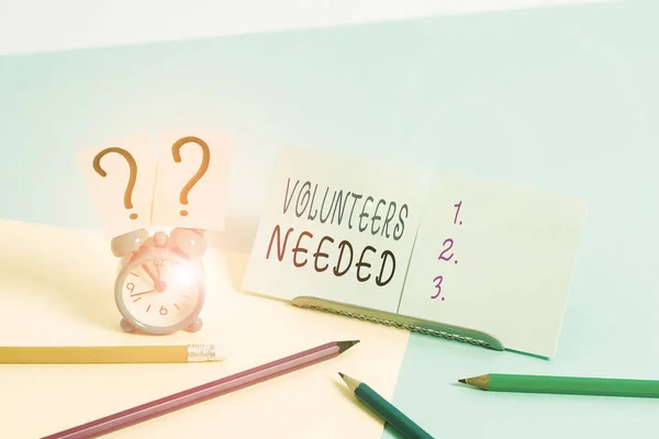 Writing note showing Volunteers Needed. Business photo showcasing need work or help for organization without being paid Mini size alarm clock beside stationary on pastel backdrop. — Stock Photo, Image