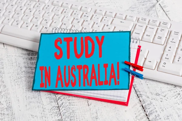 Handschrift tekst Studeren in Australië. Concept betekent gaan in het buitenland orde voltooien van uw studies notebook papier herinnering wasknijper spelden blad wit toetsenbord licht houten. — Stockfoto