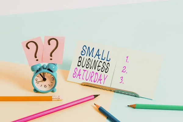 Escrevendo uma nota mostrando Small Business Saturday. Foto de negócios mostrando feriado americano de compras realizadas durante o sábado Mini tamanho despertador ao lado estacionário em pano de fundo pastel . — Fotografia de Stock