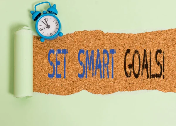 Word writing text Set Smart Goals. Business concept for list to clarify your ideas focus efforts use time wisely Alarm clock and torn cardboard placed above a wooden classic table backdrop.