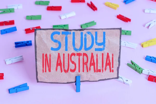 Handwriting text writing Study In Australia. Concept meaning going into foreign country order complete your studies Colored clothespin papers empty reminder pink floor background office pin.