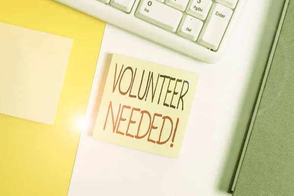 ボランティアの必要性を示すテキスト記号。支払いなしで組織のために働くことを示す概念的な写真オレンジの背景テーブルの上にコピースペースとPCキーボードを持つ空の空白の紙. — ストック写真
