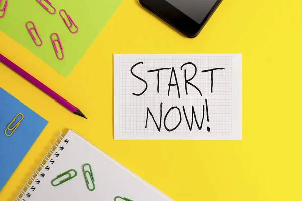 Escribir nota mostrando Start Now. Exhibición de fotos de negocios no dude en ponerse a trabajar o hacer cosas de inmediato hojas de papel cuaderno cuadrado clips lápiz teléfono inteligente de color de fondo . — Foto de Stock