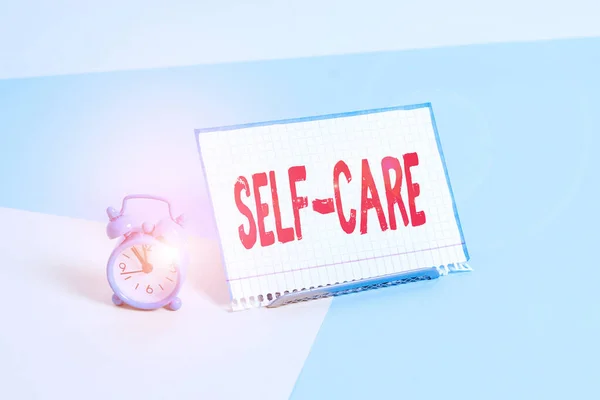 Word writing text Self Care. Business concept for practice of taking action to preserve or improve ones own health Mini size alarm clock beside a Paper sheet placed tilted on pastel backdrop. — Stock Photo, Image