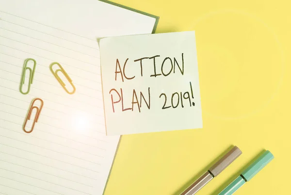 Word writing text Action Plan 2019. Business concept for proposed strategy or course of actions for current year Empty blue paper with copy space paper clips and pencils on the yellow table.