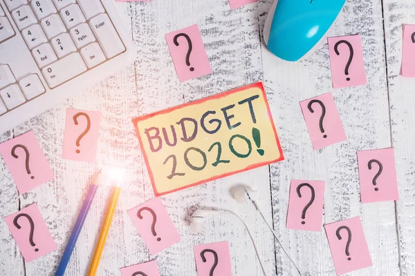 Handwriting text writing Budget 2020. Concept meaning estimate of income and expenditure for next or current year Writing tools, computer stuff and scribbled paper on top of wooden table.
