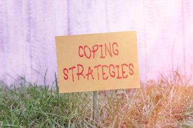 Coping Stratejilerini gösteren bir not yazıyorum. Ticari fotoğraf sergilenen genel plan ya da bir şeyler başarmak için planlar. Çimenli topraklara sade kağıt iliştirilmiş..