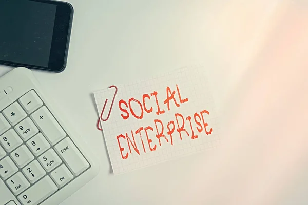 Handwriting text Social Enterprise. Concept meaning It is a business that has specific civil objectives White pc keyboard with empty note paper above white background and mobile phone.