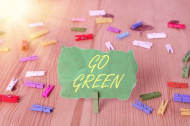 Kelime yazma metni Go Green. Daha çevre dostu bir yaşam tarzı ve karar verme konsepti Renkli çamaşır iğnesi kağıtları boş hatırlatıcı ahşap zemin ofis.