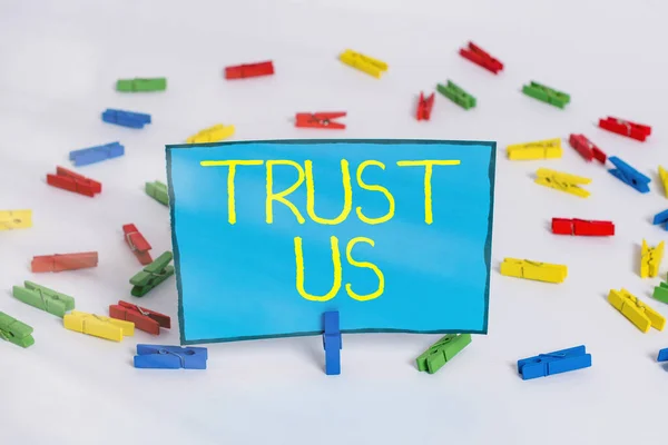 Word writing text Trust Us. Business concept for believing in the integrity and honesty of a larger scale of population Colored clothespin papers empty reminder white floor background office.