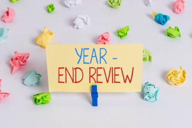 Yıl sonu incelemesini gösteren kavramsal el yazısı. İş fotoğrafında yıllık başarı ve hedef geliştirme değerlendirmesi gösteriliyor. Renkli buruşmuş kağıt boş hatırlatıcı beyaz zemin mandalı.