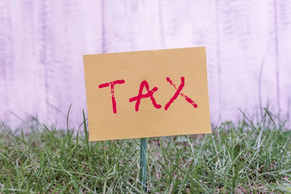 Schrijfbriefje met belasting. Bedrijfsfoto presentatie verplichte financiële last opgelegd aan de belastingbetaler door de overheid Plain papier bevestigd aan stok en geplaatst in het grasland. — Stockfoto