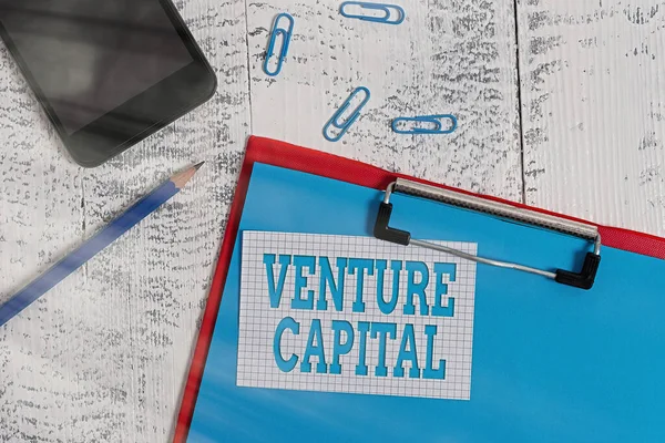 벤처 캐피탈 (Venture Capital) 에서 글을 쓴다. 새로운 클립보드 종이 연필 메모에 대한 투자에 대한 개념적 의미 스마트 폰 오래 된 나무 배경. — 스톡 사진