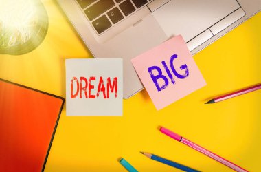 Dream Big 'i gösteren bir not yazıyorum. İş fotoğraflarında olumlu bir tavır sergiliyoruz. Yüksek hedefler peşinde koşmak ve başarmak için motivasyon sağlıyoruz. Laptop notları, konteyner not defterleri, kalemler renkli.