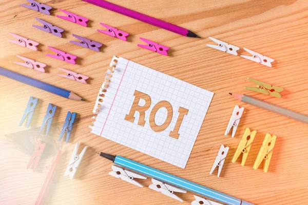 Writing note showing Roi. Business photo showcasing performance measure used to evaluate the efficiency of an investment Colored clothespin papers empty reminder wooden floor background office.