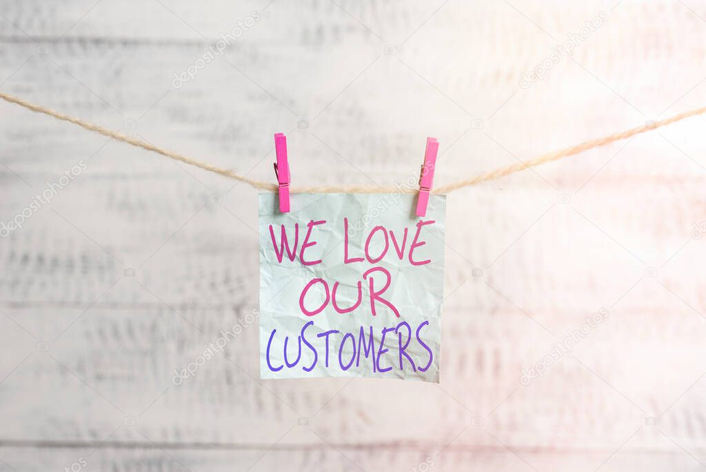 Writing note showing We Love Our Customers. Business photo showcasing clients care and attention Good customer services Clothesline clothespin rectangle shaped paper reminder white wood desk.
