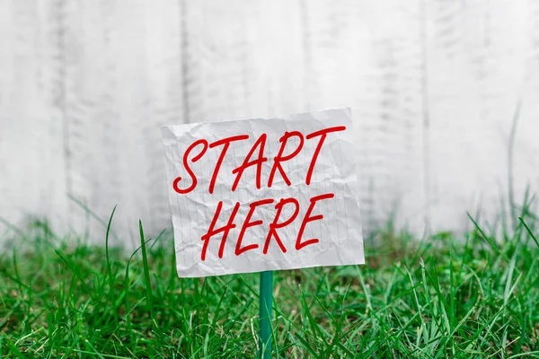 Conceptual hand writing showing Start Here. Business photo showcasing an act of pointing a location or portion on where to start Plain paper attached to stick and placed in the grassy land.