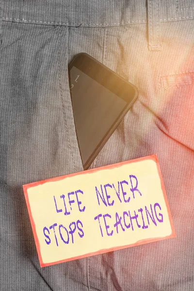 Tekst pisma Życie nigdy nie przestaje uczyć. Koncepcja oznacza zachować techniki uczenia się Poszukaj sposobów, aby poprawić urządzenie Smartphone wewnątrz formalnej kieszeni spodni roboczych w pobliżu papieru notatkowego. — Zdjęcie stockowe