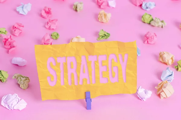 Escribir texto a mano Estrategia. Concepto que significa plan de acción o estrategia diseñada para lograr un objetivo general Papeles arrugados coloreados recordatorio vacío pinza de ropa de fondo de piso rosa . — Foto de Stock