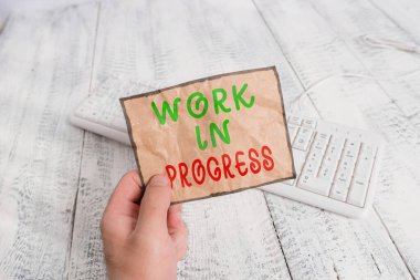 Çalışmanın İlerlediğini gösteren kavramsal el yazısı. İş fotoğrafı metni: Takım çalışması, strateji ve iş birliği yapan adam elinde renkli hatırlatıcı kare şeklindeki kağıt ahşap zemin tutuyor..