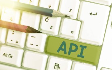 Api 'yi gösteren kavramsal el yazısı. Rutinlerin, protokollerin ve yazılım uygulamalarının oluşturulması için beyaz pc klavyeli beyaz nota kağıdının üzerinde bulunan araçların iş fotoğrafı metni kümesi.