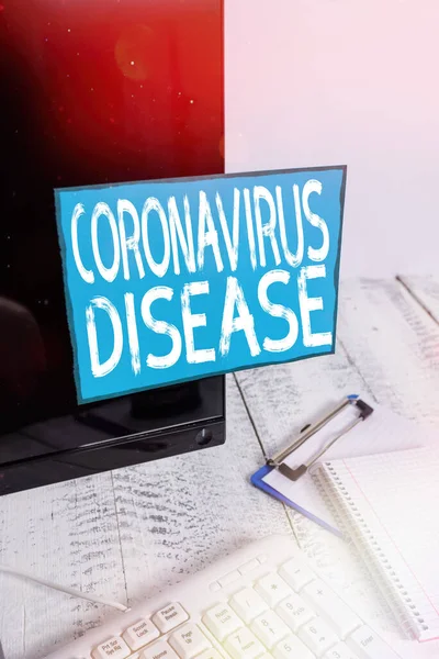 Escribiendo una nota que muestra la enfermedad por Coronavirus. Muestra de fotos de negocios definida como enfermedad causada por un nuevo virus SARSCoV2 Nota papel pegado a la pantalla del ordenador negro cerca del teclado y estacionario . —  Fotos de Stock